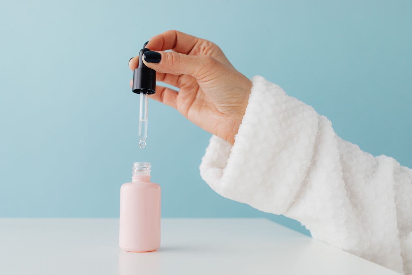 Mano dosificando sérum de un frasco rosado